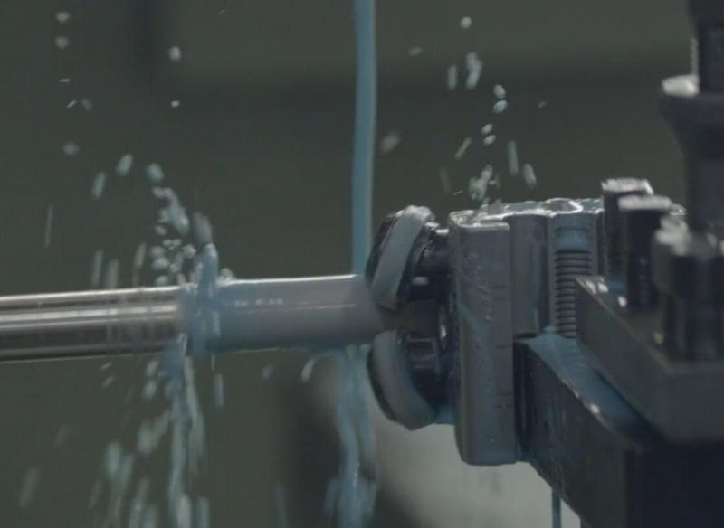 A cylindrical piece of solid brass during the machining process, with blue liquid poured from above onto the product.